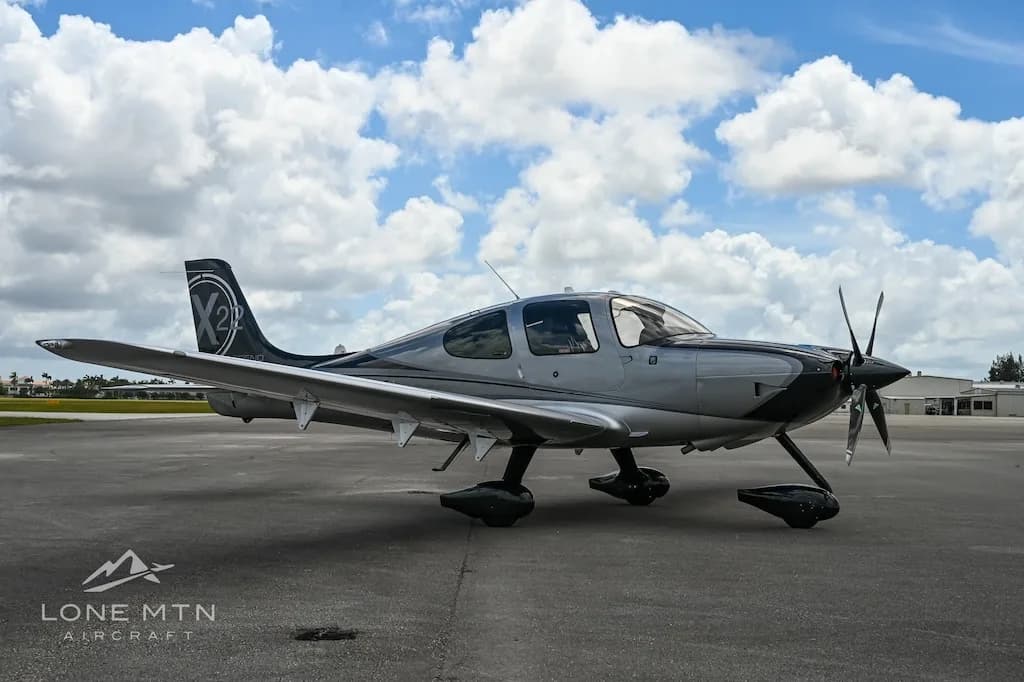 A silver and black Cirrus SR22 aircraft parked on an airfield, viewed from the front-left.