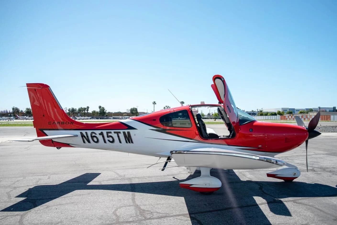 Side view of a red and white N615TM aircraft with its doors open, parked on an airfield.