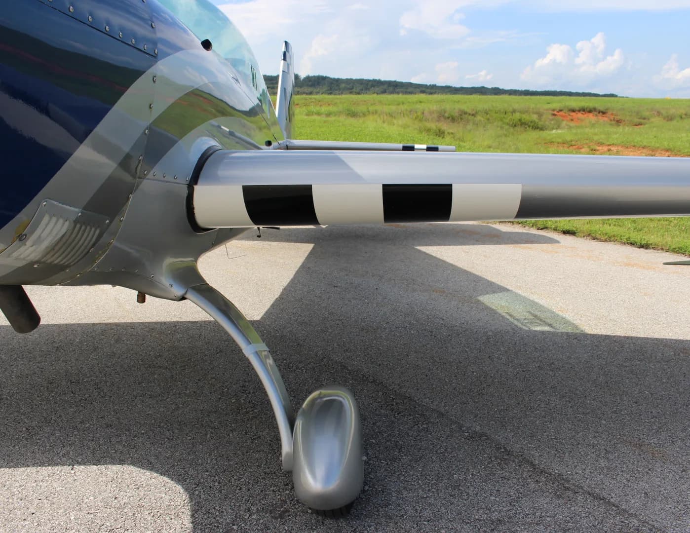 A side view of the landing gear and wing root of the N51E Extra EA-300/L, featuring black and white striped accents on the wing.