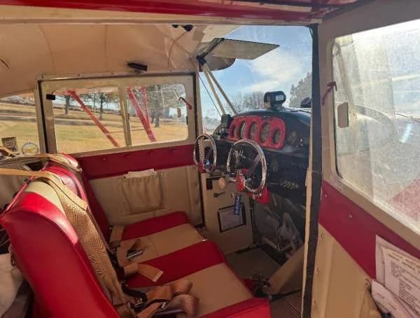 The interior cabin of an aircraft, showing red and cream striped seats and the cockpit area.