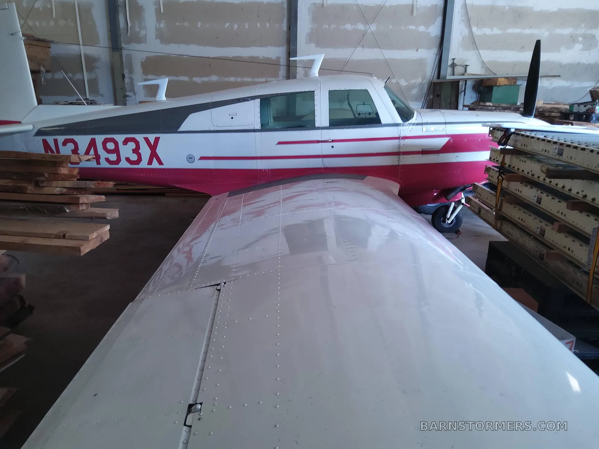 Side view of a white and red single-engine aircraft with registration N3493X, parked in a hangar.