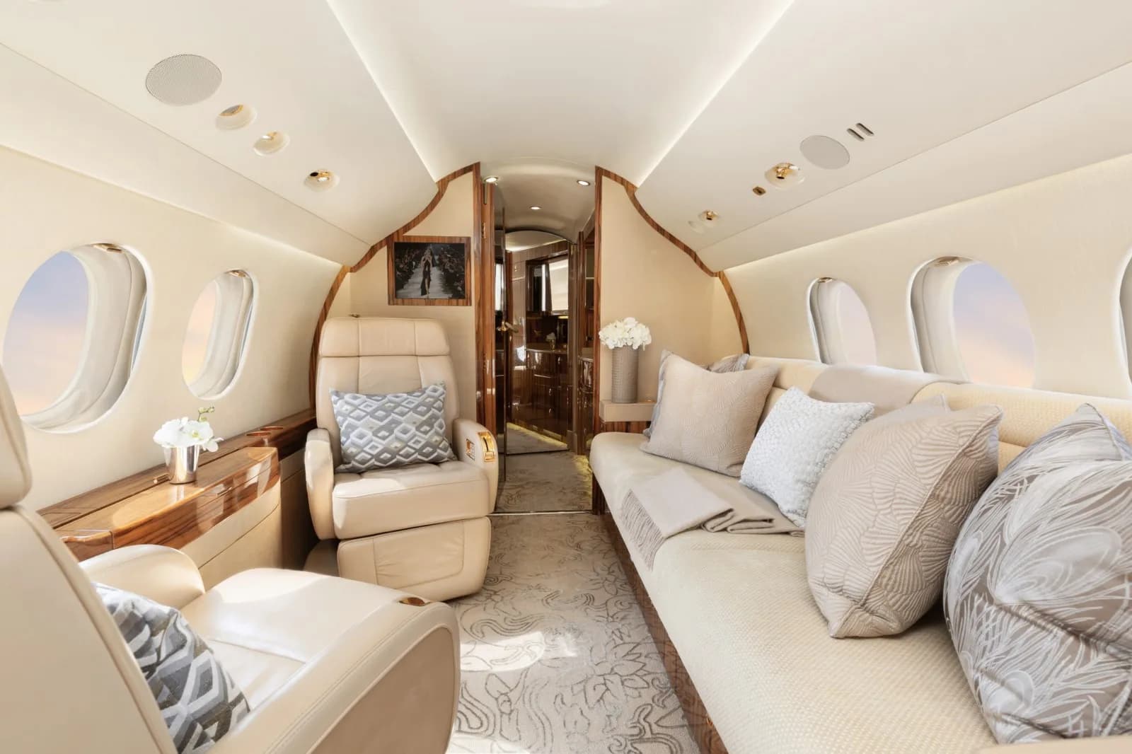 A luxurious aircraft cabin with a long cream sofa, individual seats, and a patterned carpet.
