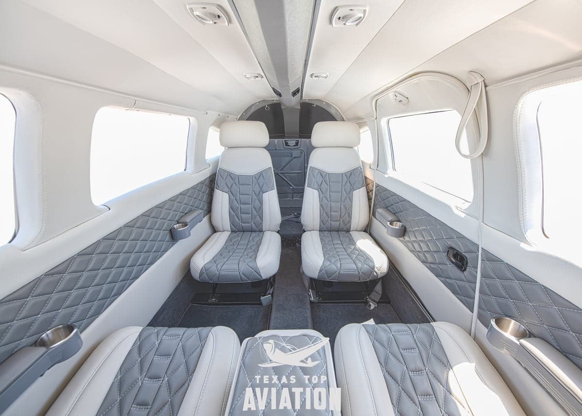 The interior of an aircraft cabin features gray and white leather seats.
