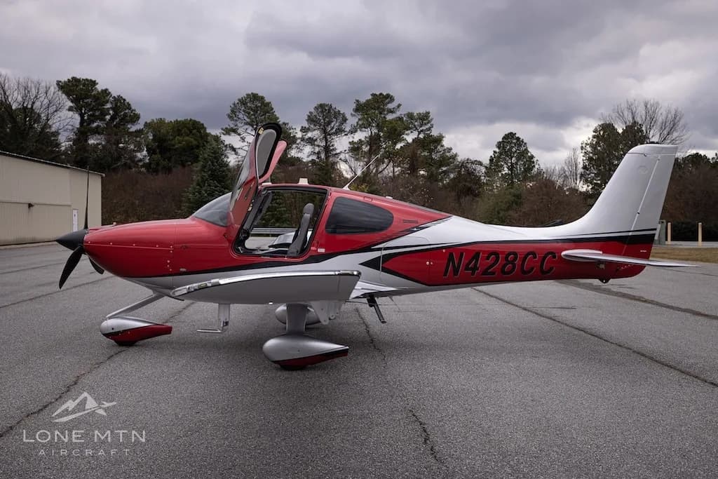 A side view of the red and silver Cirrus Vision Jet (N428CC) with its doors open, parked on an asphalt tarmac.