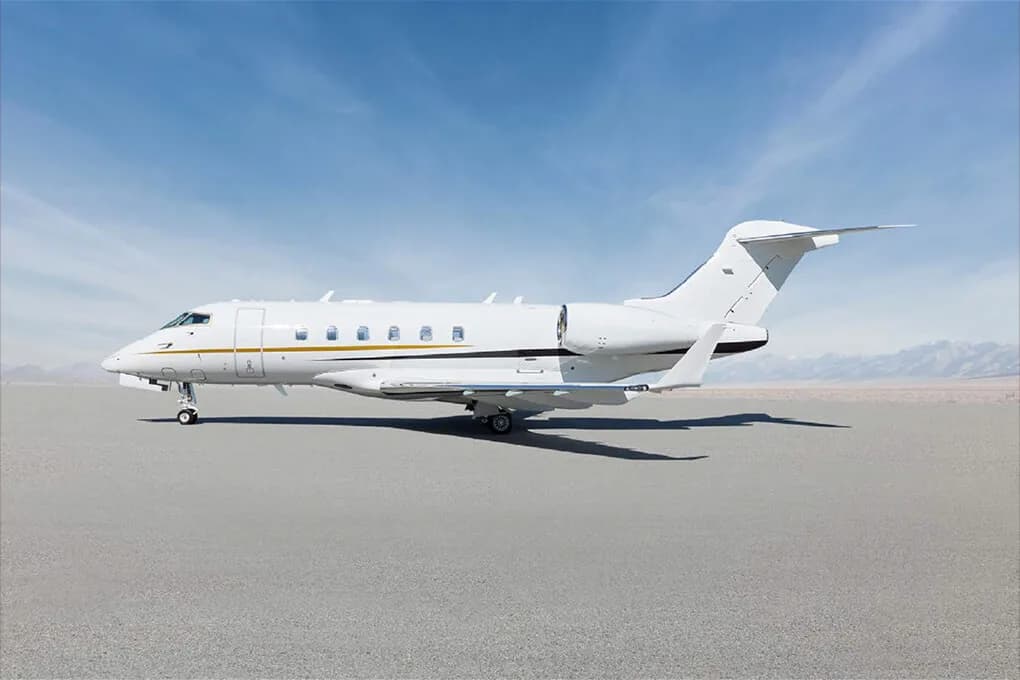 A white business jet with gold accent stripes parked on an airfield under a clear blue sky.