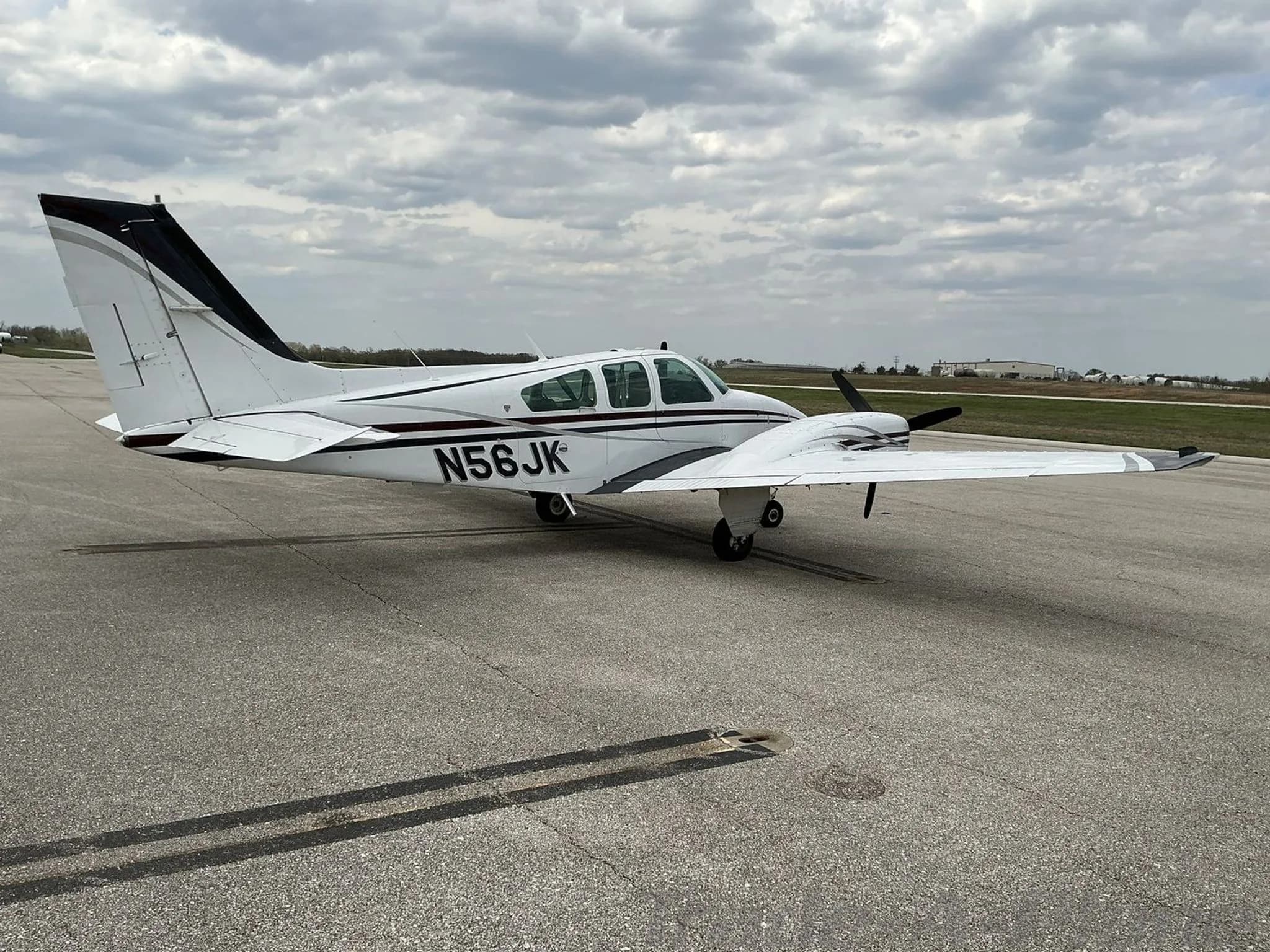 A front-side view of a white twin-engine propeller aircraft with N56JK tail number, black and maroon stripes, parked on an asphalt tarmac.