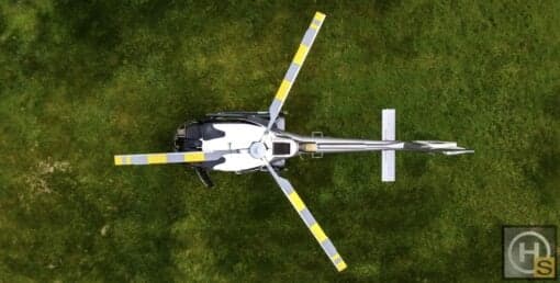 Aerial view of a grey and white helicopter on a grassy field.