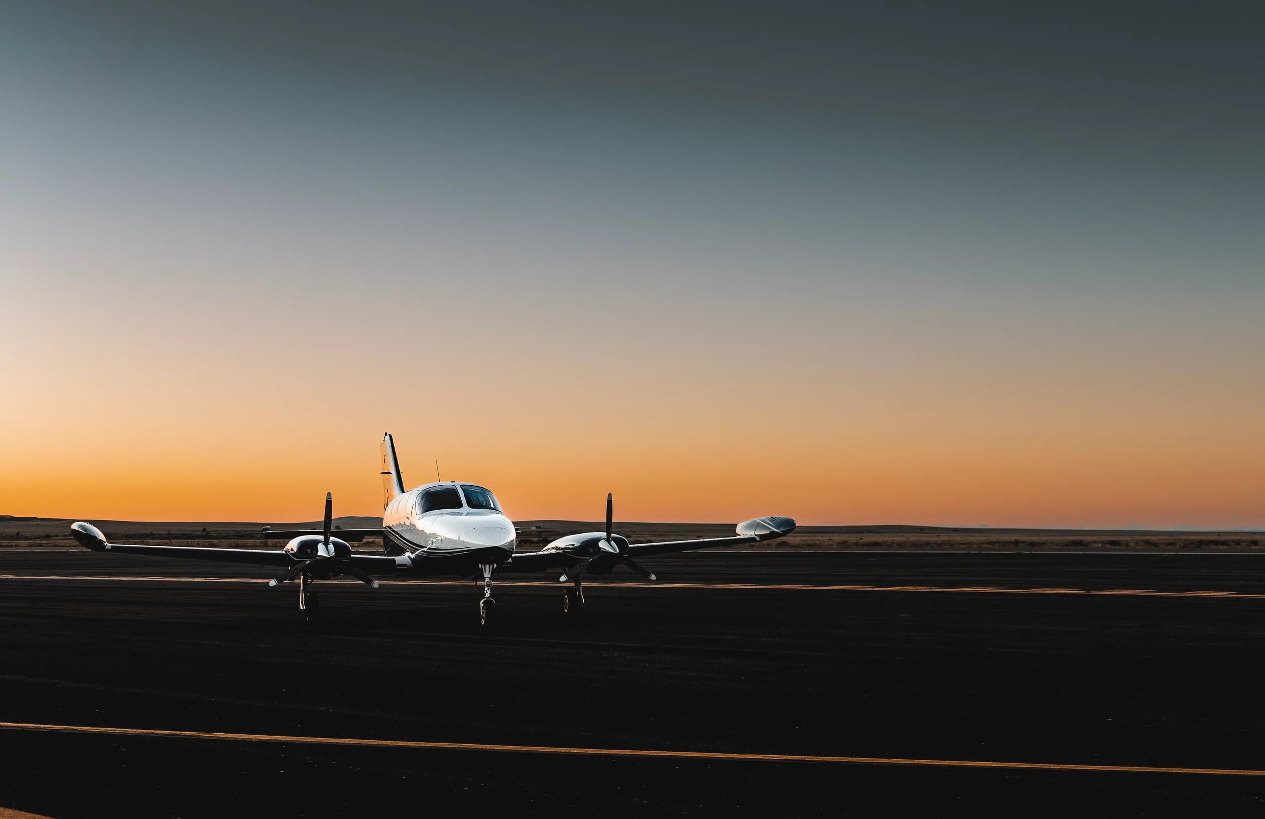 A white and black twin-engine aircraft parked on a runway at sunset.