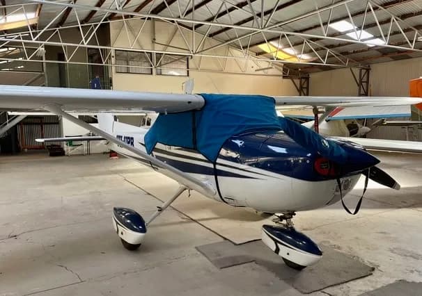 A white and blue single-engine propeller aircraft with a blue cover on its nose and canopy, parked inside a hangar.