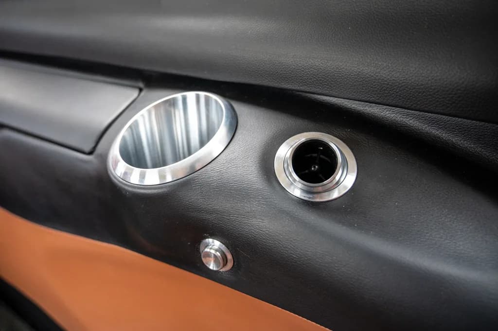 A close-up of an aircraft interior panel showing a silver cup holder and an air vent.