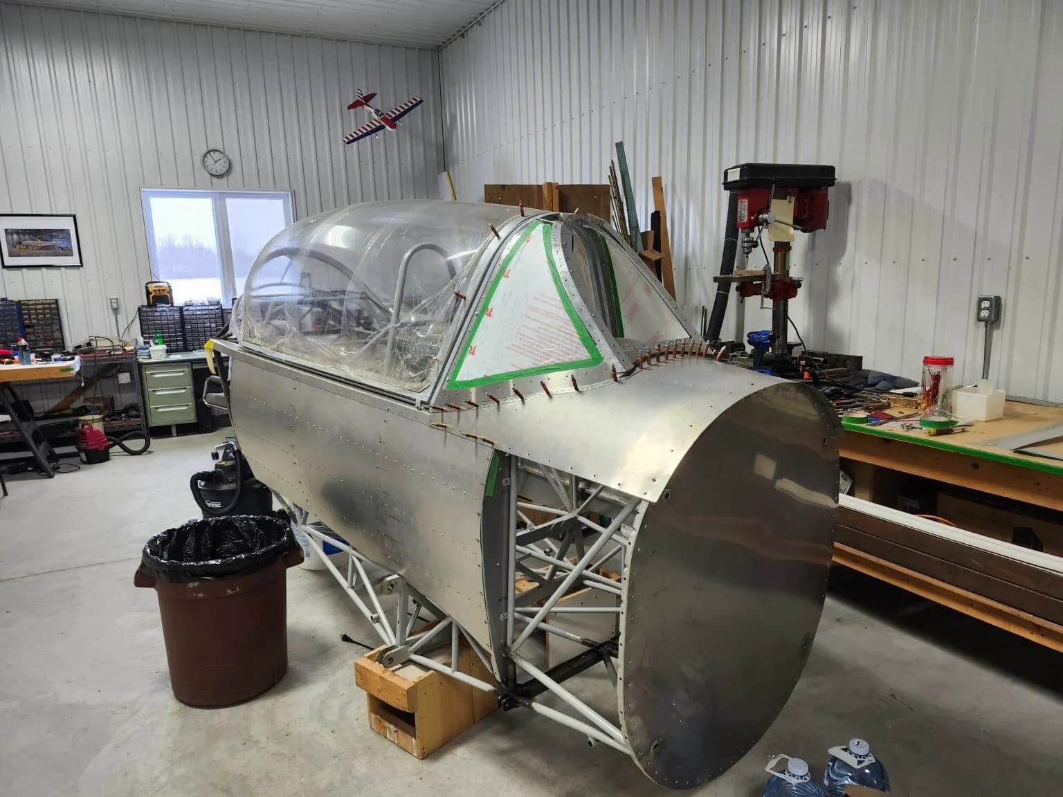 The front fuselage section of an aircraft, with a clear canopy installed, in a workshop setting.