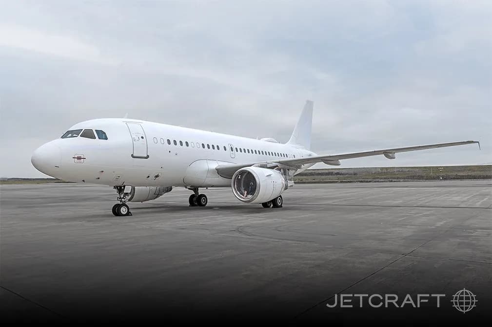 A white Airbus A319 aircraft parked on an airport tarmac under a cloudy sky.