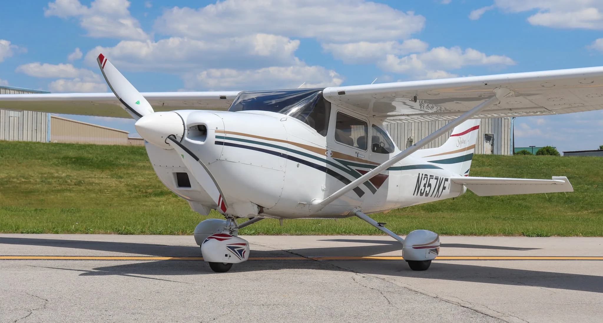 A front-quarter view of a white Cessna 182 Skylane with multi-color stripes on an airport ramp.