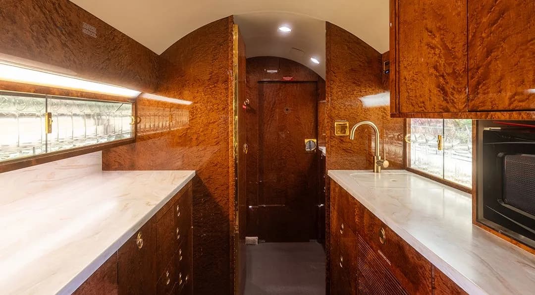 The galley of the business jet, featuring marble countertops, wood cabinetry, a sink, and a microwave.