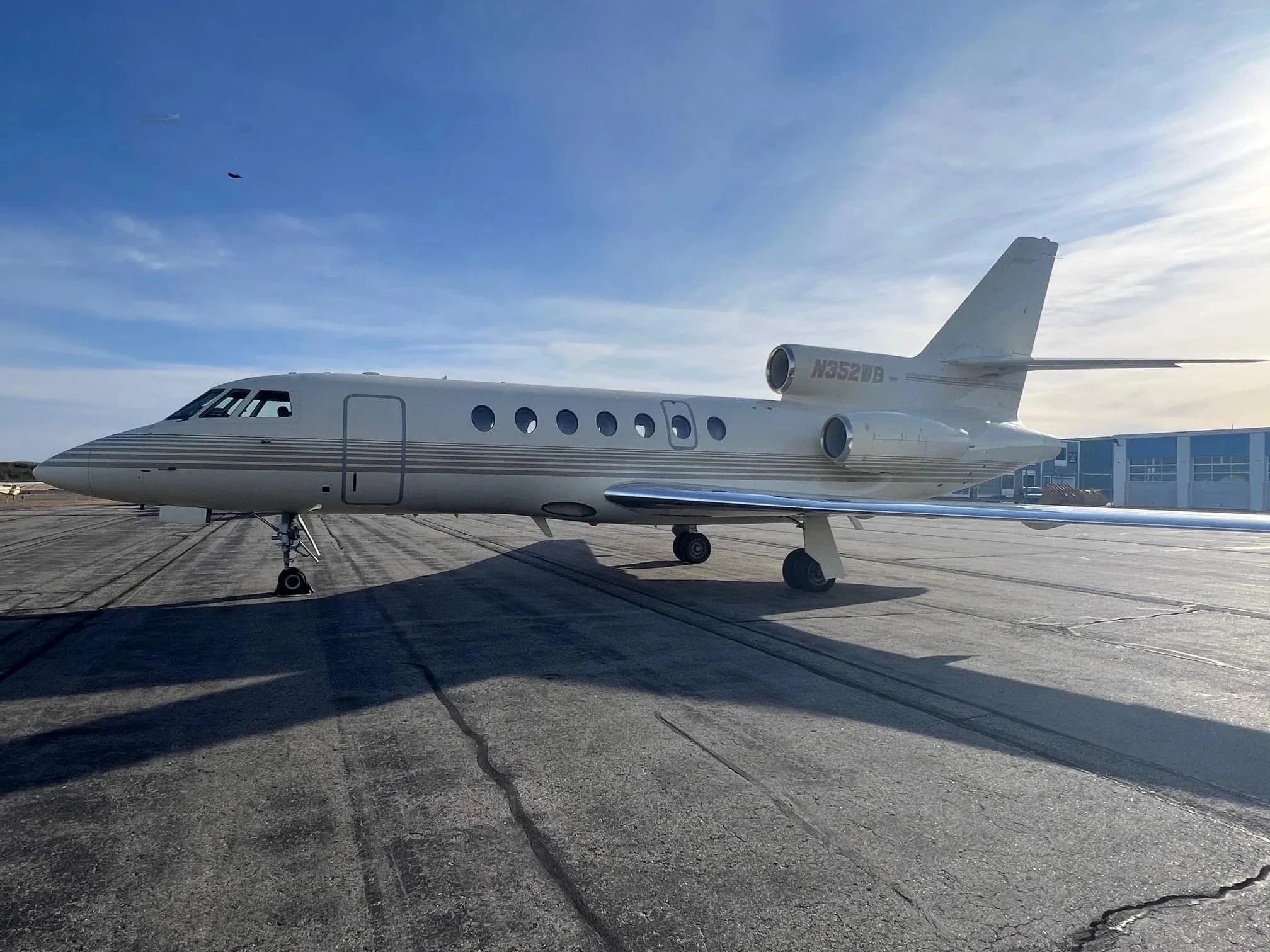 A beige Dassault Falcon 900EX business jet with N352WB registration on the tail, parked on an airport tarmac at sunset.