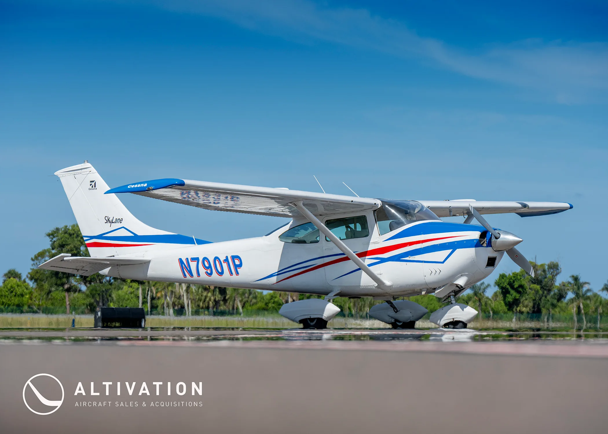 A side view of a white Cessna 182 Skylane with blue and red stripes parked on a tarmac.
