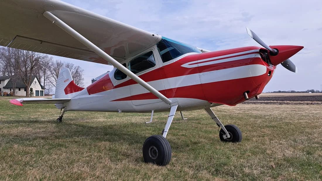 Front quarter view of a red and white Cessna on a grassy field.