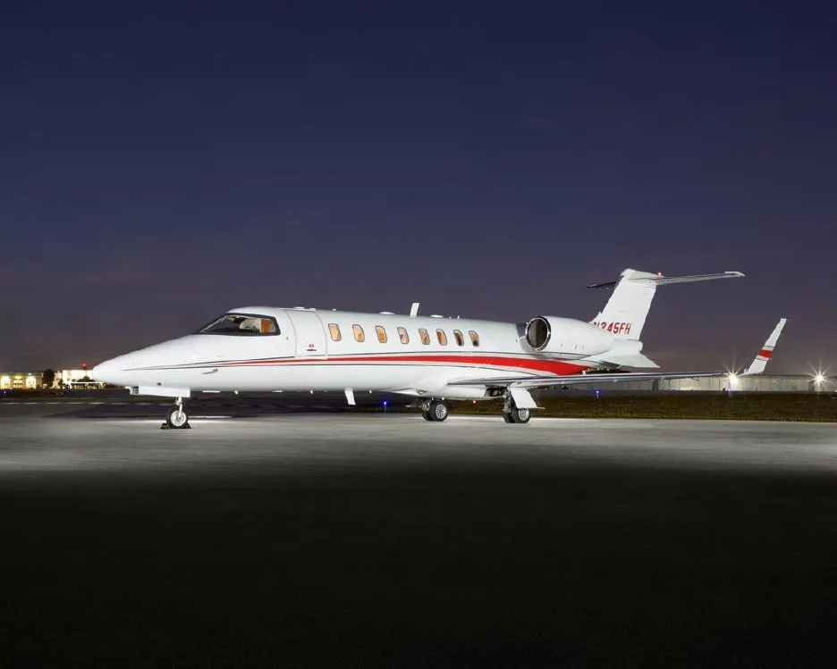 A white and red Learjet on the tarmac at night.