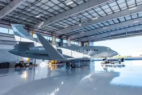 The Dassault Falcon 2000S business jet, registration N215FH, in matte grey, parked inside a brightly lit hangar.