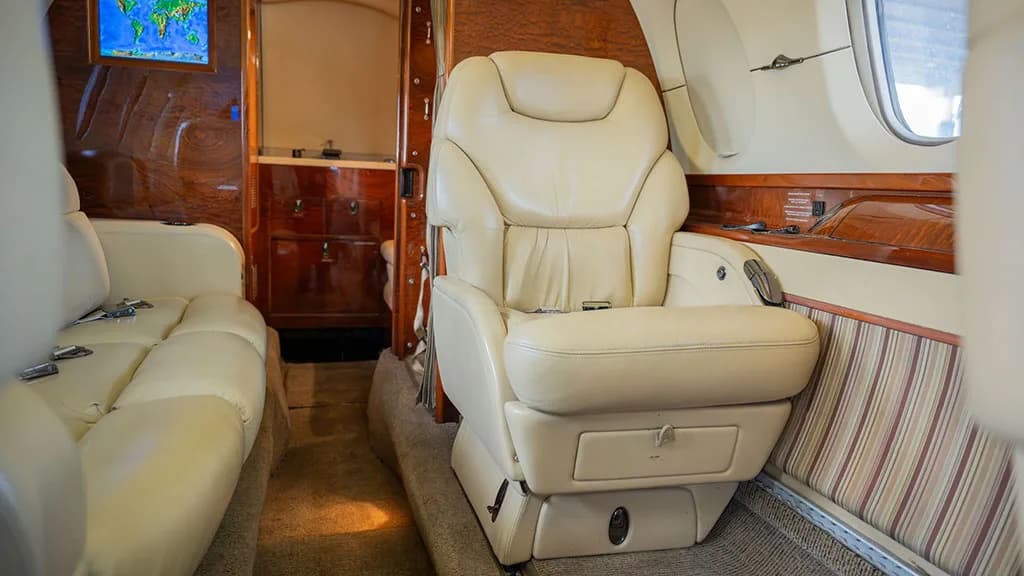 A cream leather single seat in the private jet cabin, with wood paneling and a world map display in the background.