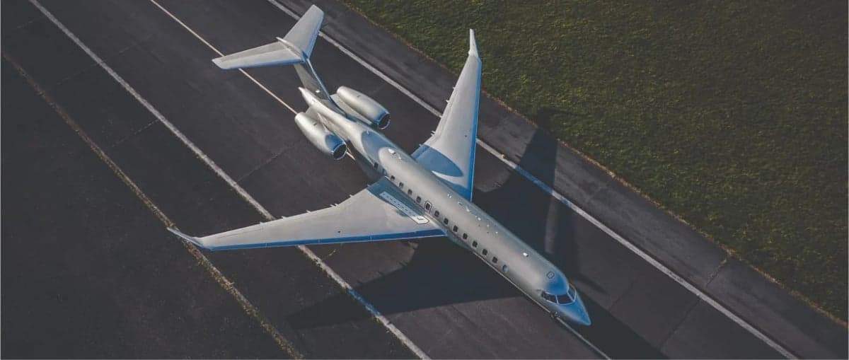 An aerial view of a silver business jet with a blue stripe on a runway.