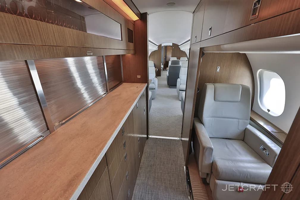 The galley area of a Bombardier Global 6000, with wooden cabinetry, a countertop, and a view into the main cabin.