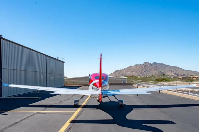A rear view of the red and silver Cirrus SR22T GTS Carbon aircraft parked on an airfield with mountains in the background.