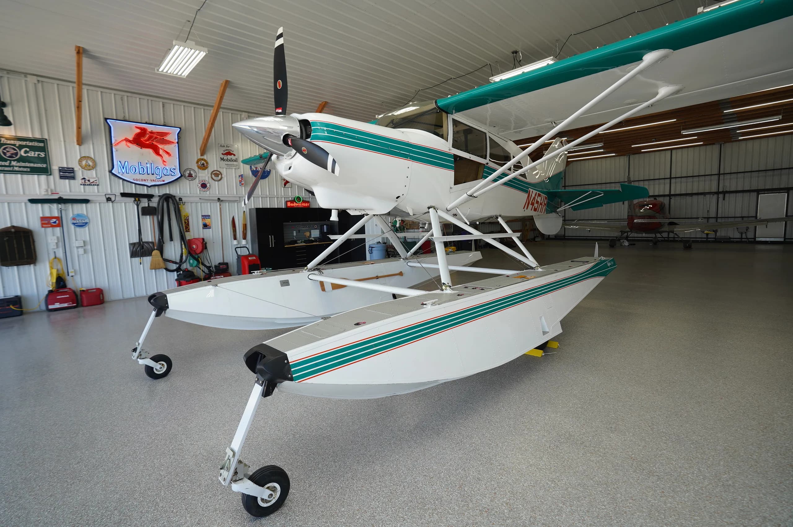 Front-left view of a white and teal floatplane with wheels, parked in a hangar.