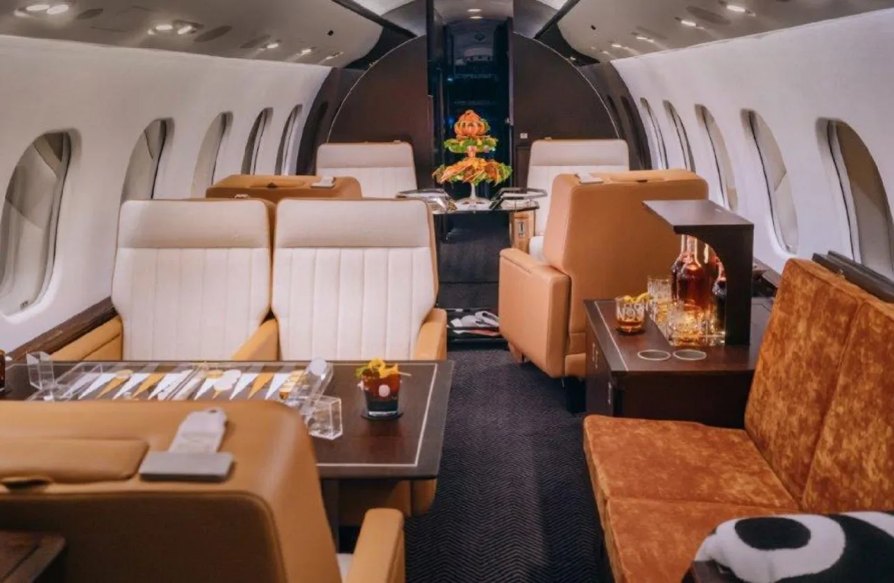 A spacious view of the private jet's cabin, showing multiple seating arrangements, a dining table with a backgammon set, and a bar area.