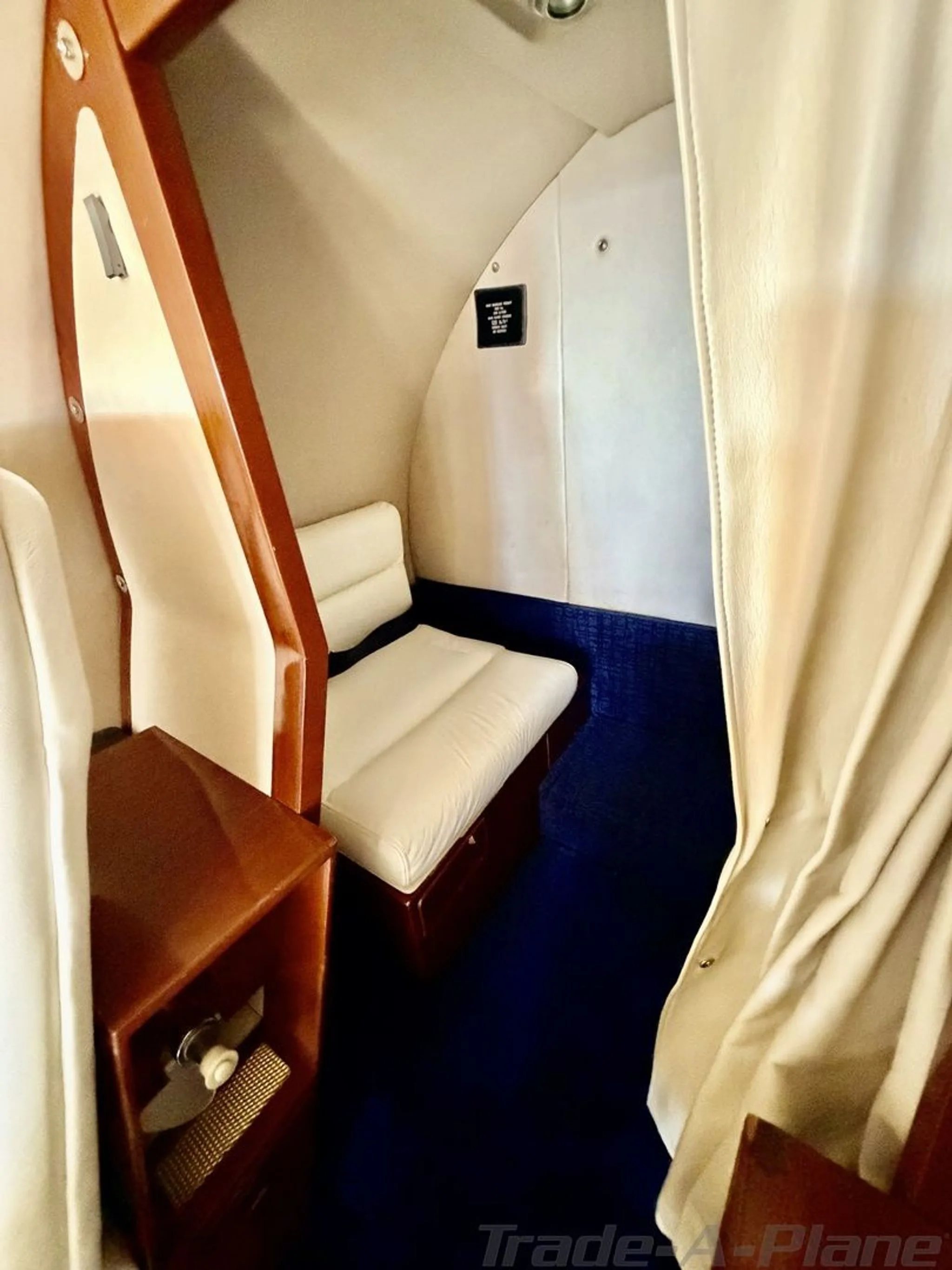 A view of the aircraft's interior cabin, showing a cream-colored bench seat, wooden trim, and a privacy curtain.