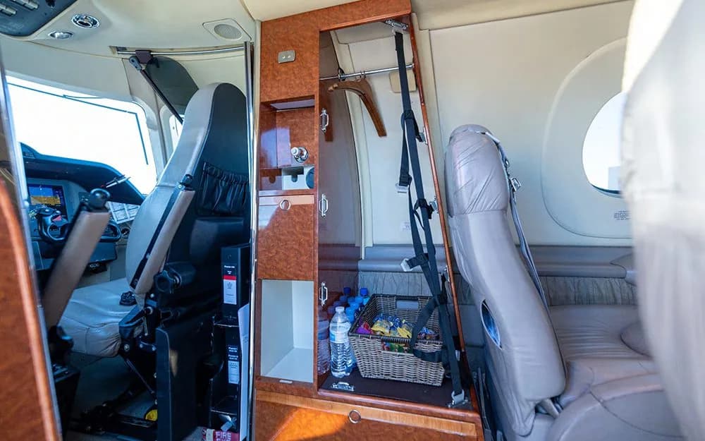 A view inside the aircraft cabin showing a wood-paneled storage unit with a small basket of snacks and a glimpse of the cockpit.