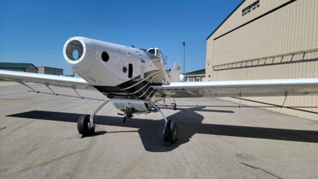 Frontal view of a white Thrush agricultural aircraft with its engine cowling open, parked on an tarmac.