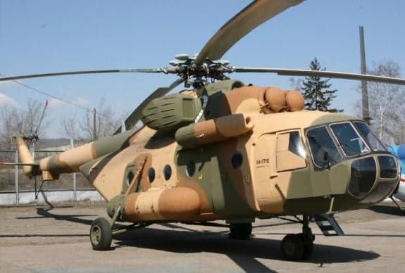 A camouflaged helicopter sits on the tarmac.