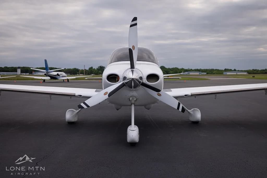 Frontal view of a white Cirrus SR22T aircraft with a three-bladed propeller parked on an asphalt tarmac.