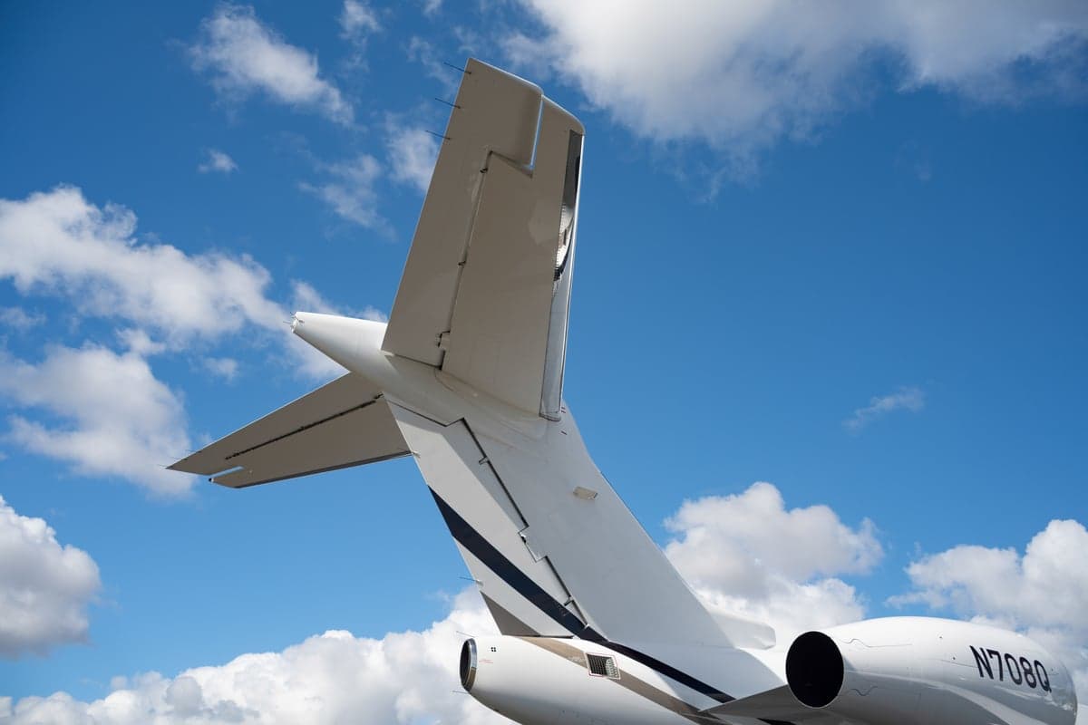 A rear view of the white tail section of a business jet with dark stripes and the registration N708Q against a blue sky.