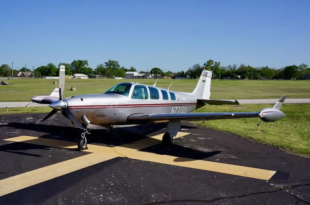 A silver and red Beechcraft Baron 58, tail number N72121, is parked on an asphalt ramp with yellow markings.