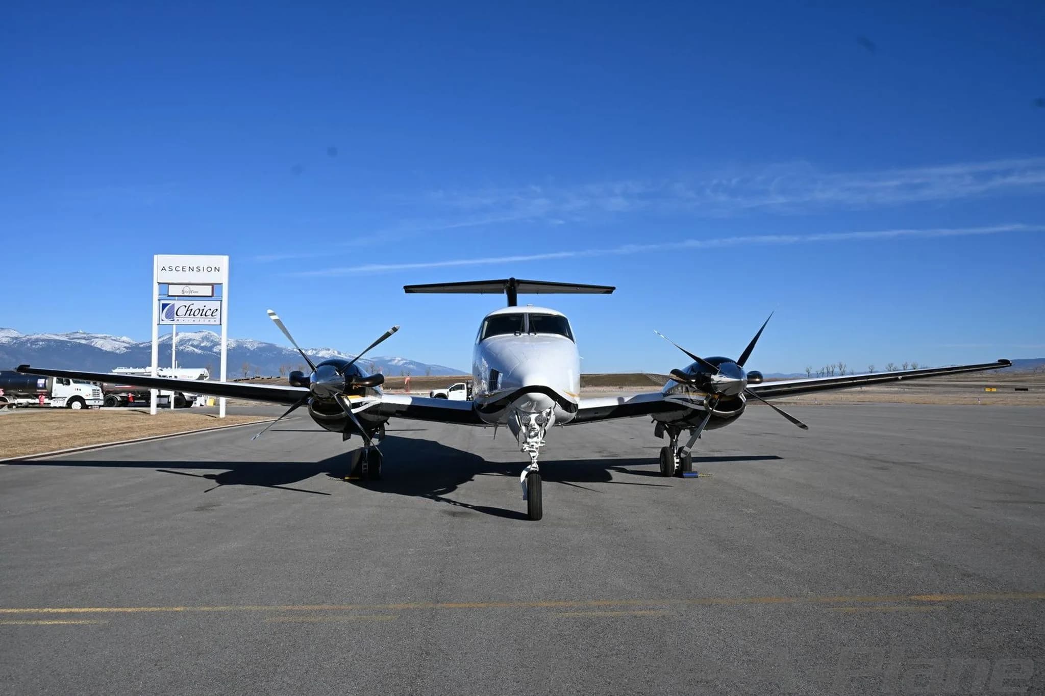 A white and black Beechcraft King Air 200 with gold stripes parked head-on on an airfield.