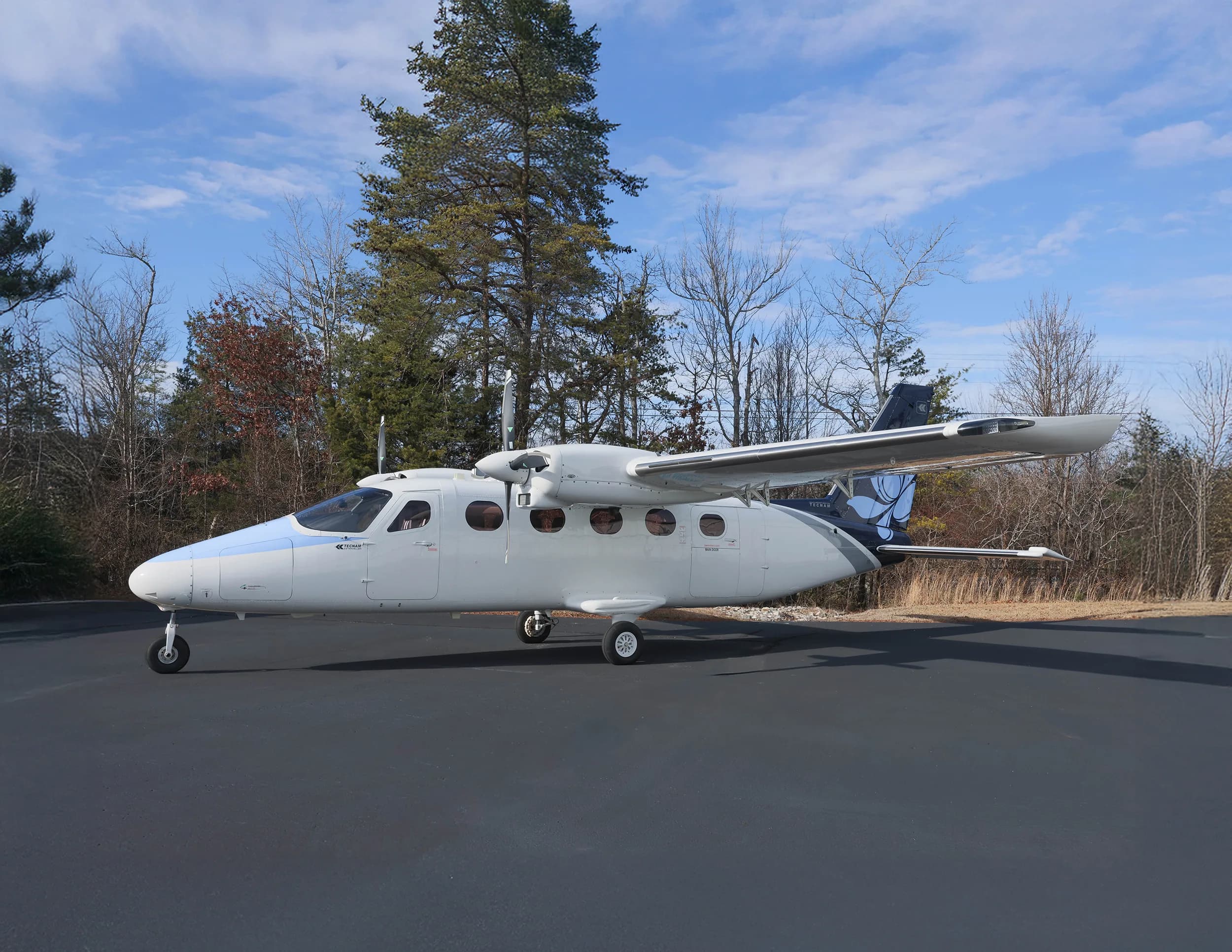 A white and blue twin-engine aircraft with a floral tail logo and registration N7700B parked on an asphalt ramp.