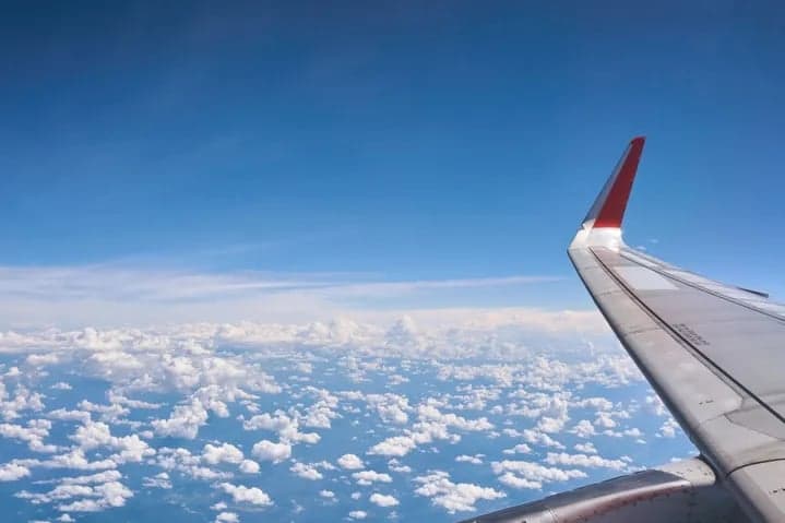 Aircraft wing in flight over clouds.