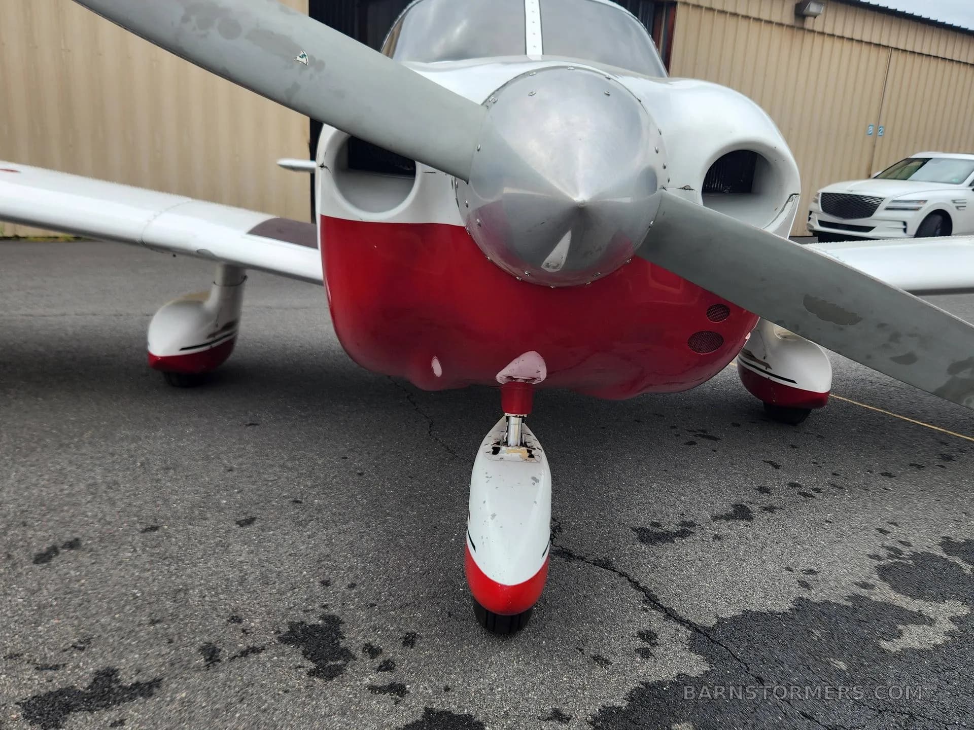 A close-up view of the front propeller and nose gear of a red and white aircraft on asphalt.