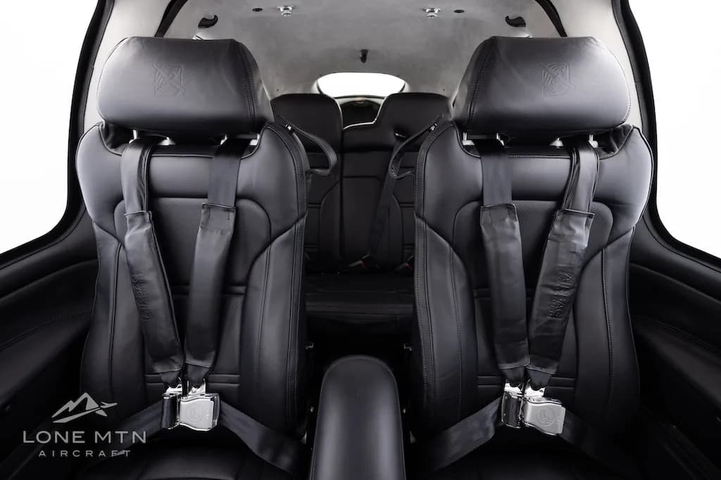 A view from the rear of the aircraft cabin, showing the black leather front and rear seats with seatbelts.