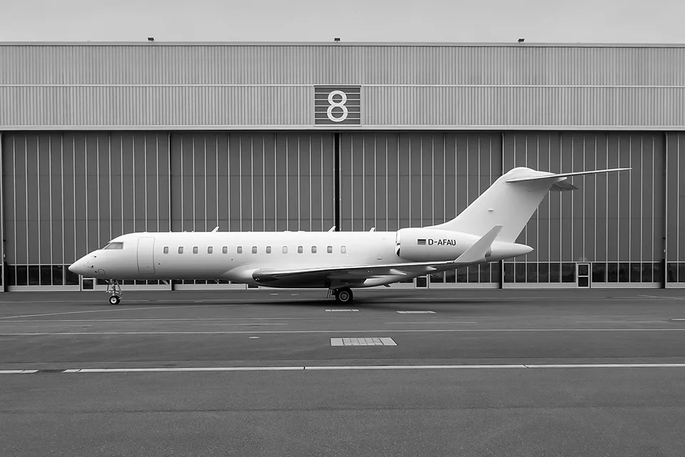 A white Bombardier Global Express business jet, registration D-AFAU, parked on the tarmac in front of a hangar.