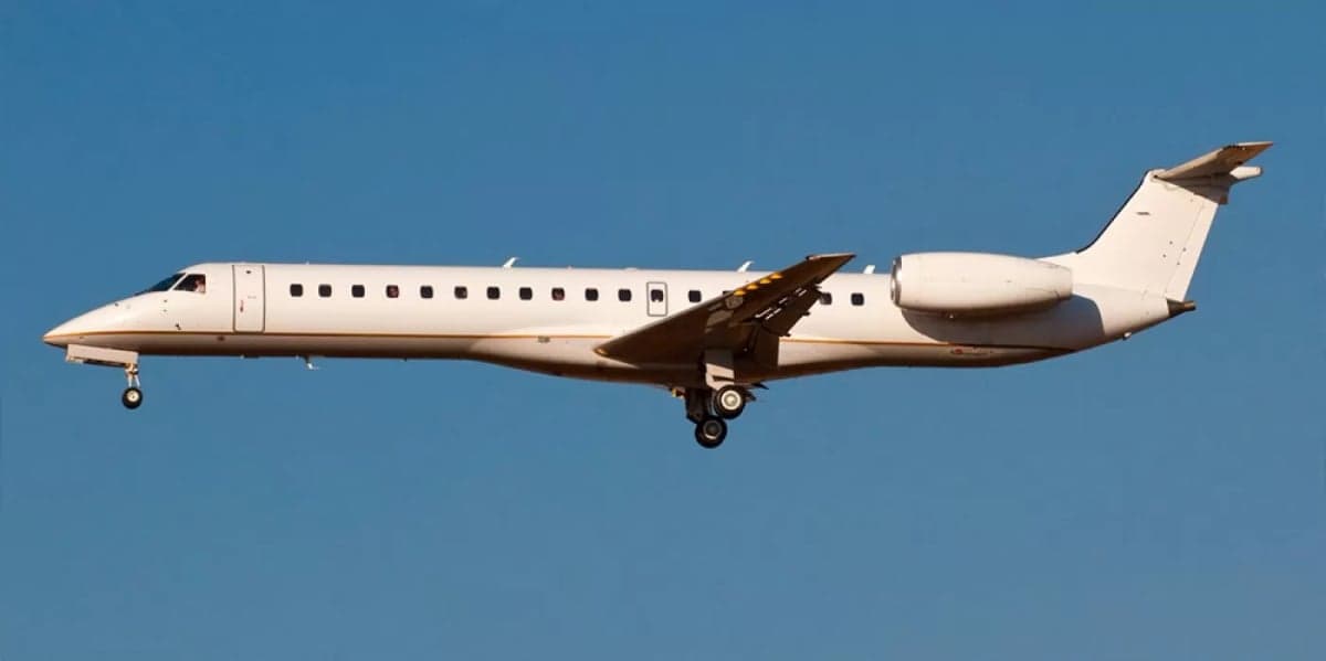 A white Embraer aircraft in flight with landing gear down.