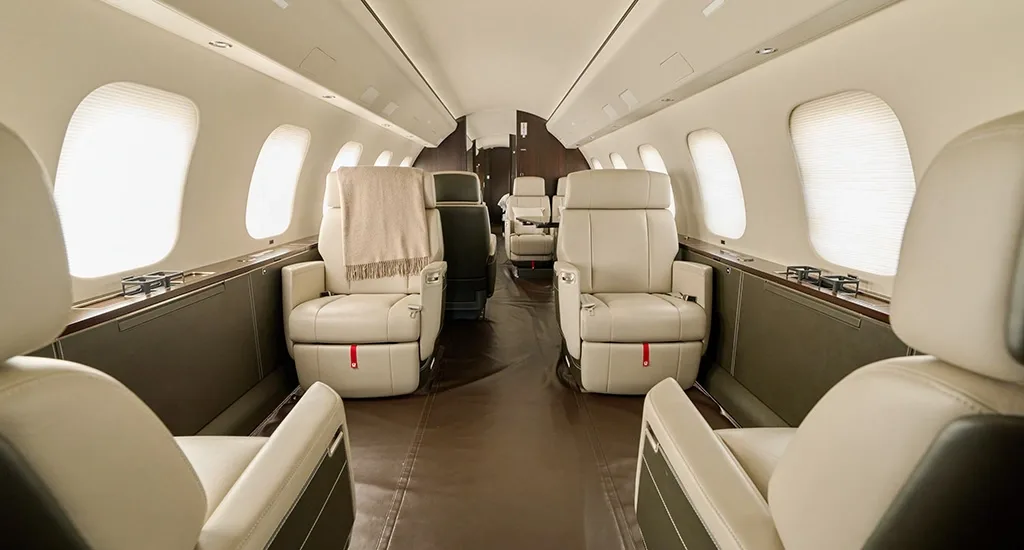 The luxurious cabin interior of a private jet with cream leather seats and dark wood accents.