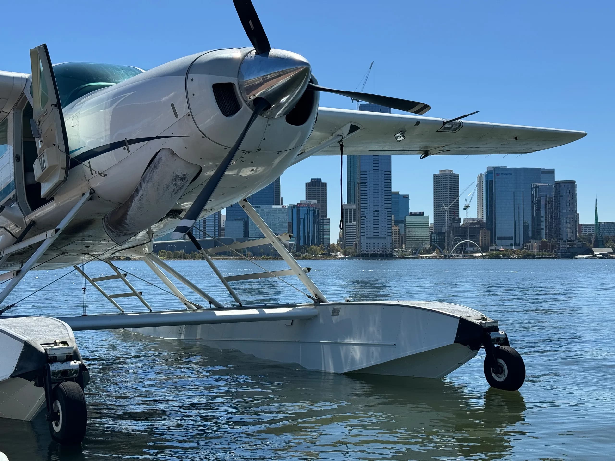 Close-up of a seaplane on the water with a city skyline in the background.