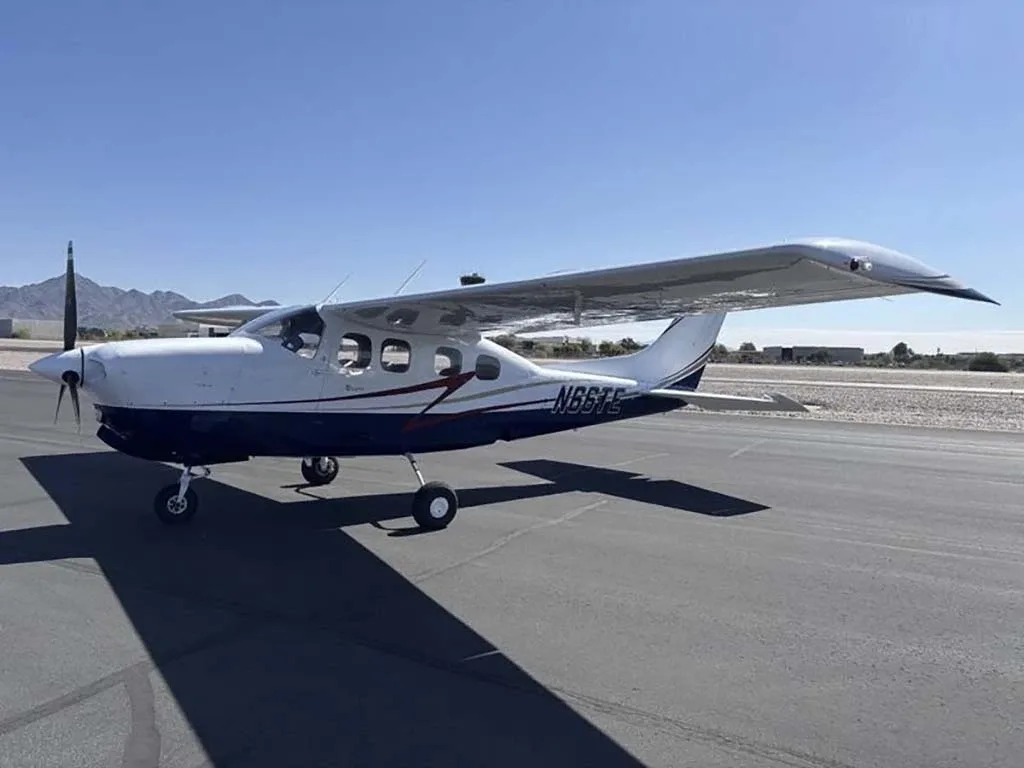 A white and blue Cessna 210 Centurion with registration N66TE parked on an airfield from a slightly different angle.