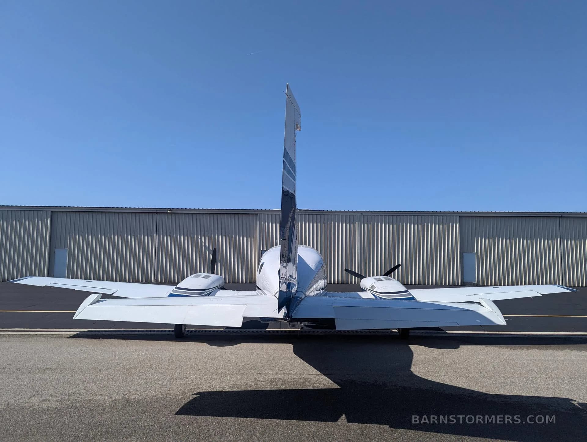 A rear view of a white and blue twin-engine propeller aircraft (Cessna 414 Chancellor) with tail number N533AC parked in front of a hangar.
