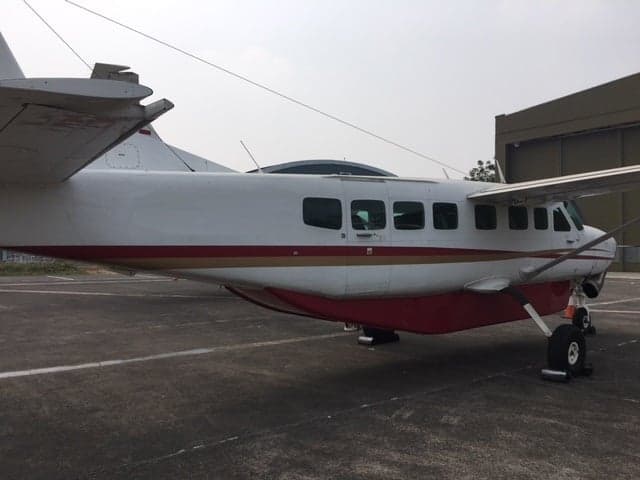 A white and red Cessna Caravan aircraft parked on an airfield, viewed from the rear-side.