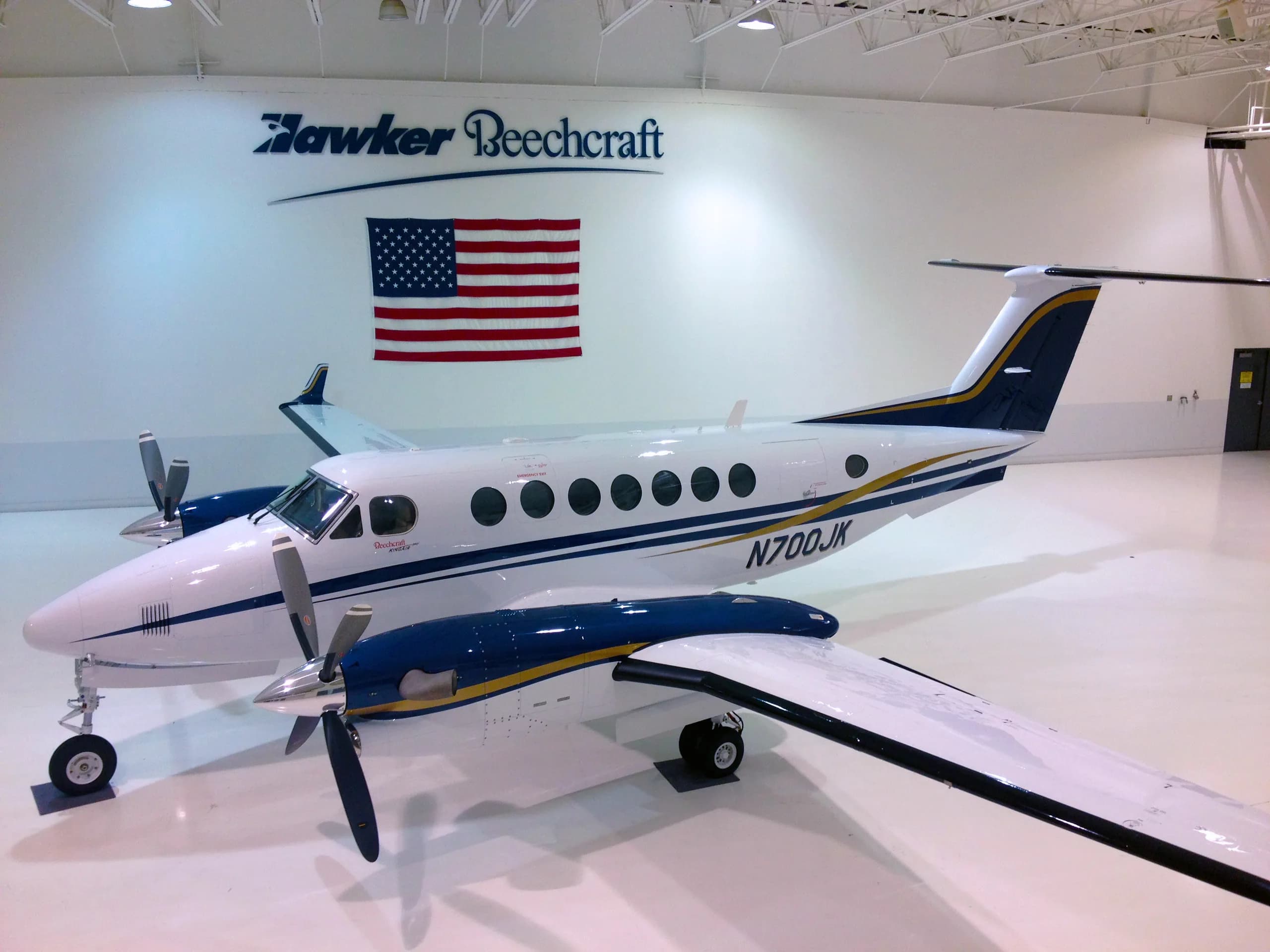 A Beechcraft King Air 350i, registration N700JK, is parked in a hangar with a Hawker Beechcraft logo and American flag in the background.