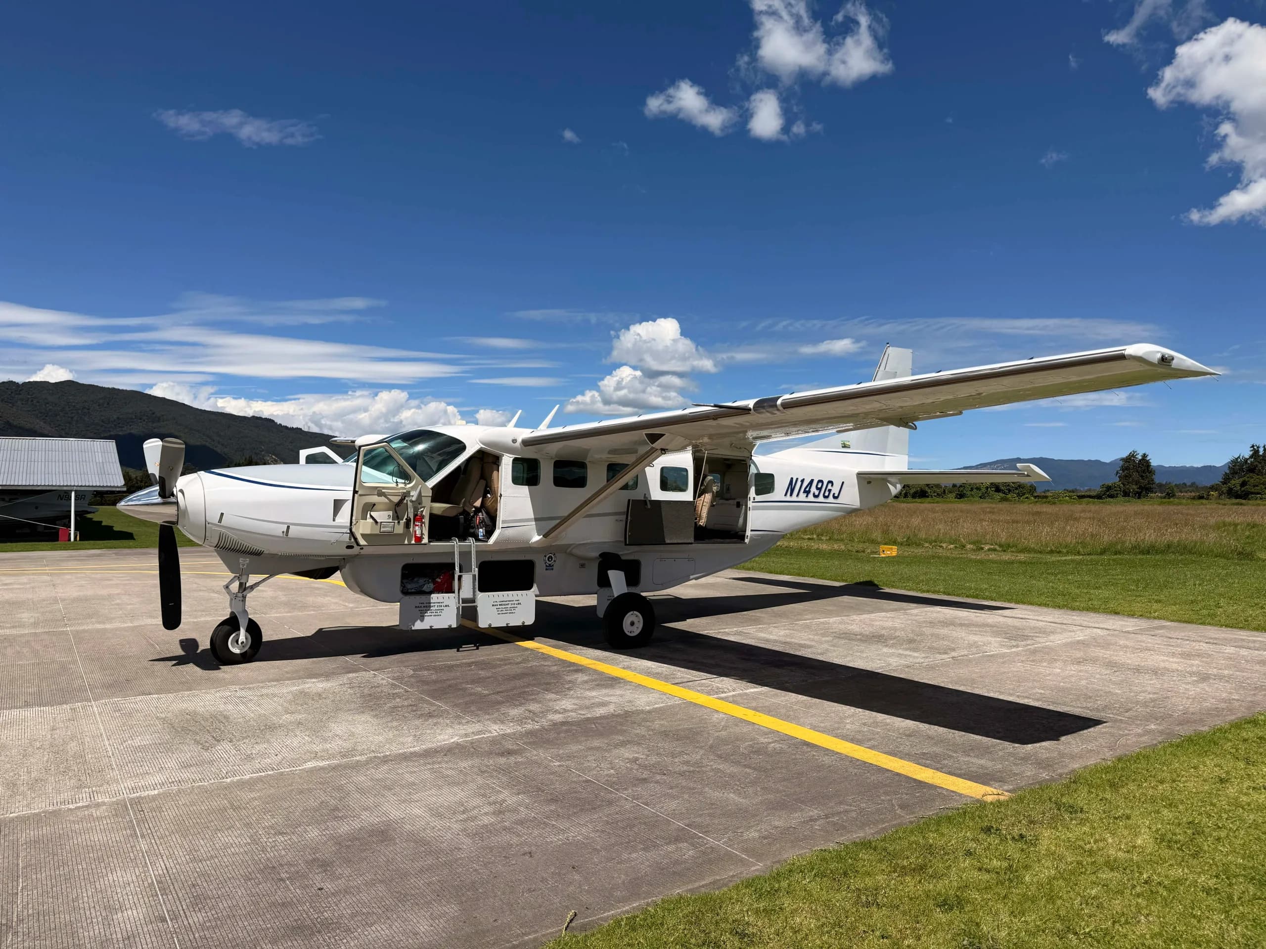 A white Cessna 180 Skywagon seaplane with green stripes is parked on a tarmac next to a hangar.